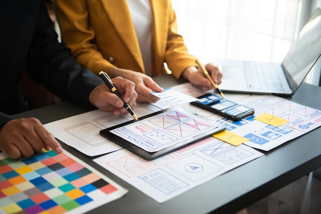 UX 開発者と ui デザイナーが、officexA で顧客の簡単な説明とカラー コードを使用して、モバイル アプリ インターフェイスのワイヤフレーム設計についてブレインストーミングを行っています。