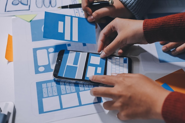 UX UI designer testing prototype on a phone discussing and brainstorming on wireframes for a website and mobile app prototype in the concept of website and mobile application design concept