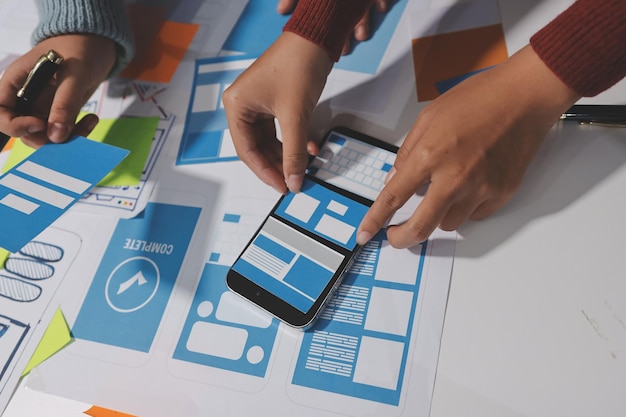 UX UI designer testing prototype on a phone discussing and brainstorming on wireframes for a website and mobile app prototype in the concept of website and mobile application design concept
