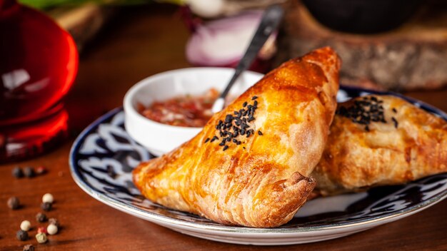 Uzbek samsa in national plate with tomato sauce on a wooden table. end of the eastern baking.