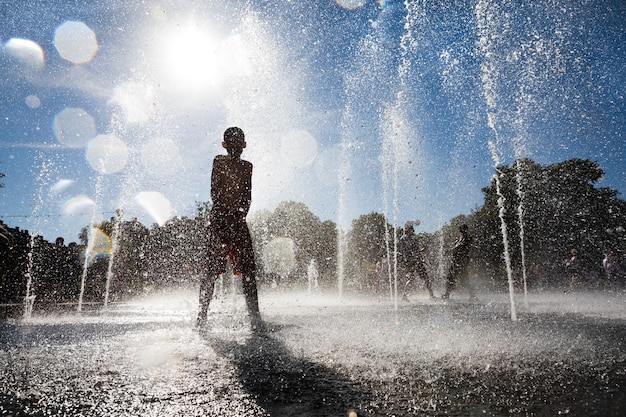 Foto uzhgorod, ucraina - 28 maggio 2017: siluetta di un adolescente che sta in una fontana e che si gode le fresche correnti d'acqua. bambini felici che giocano in una fontana d'acqua in una giornata calda