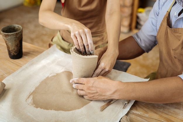 Vaas maken. Bekwame creatieve vrouw met donkere nail art potter helpen met het maken van vaas in werkplaats