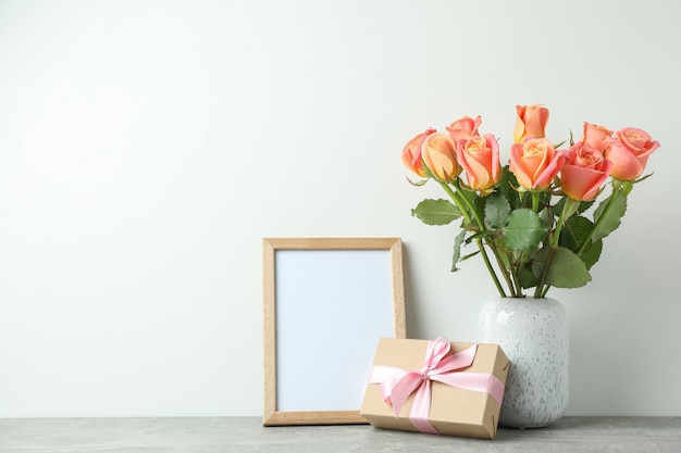 Vaas met rozen, cadeau en leeg frame op grijze tafel