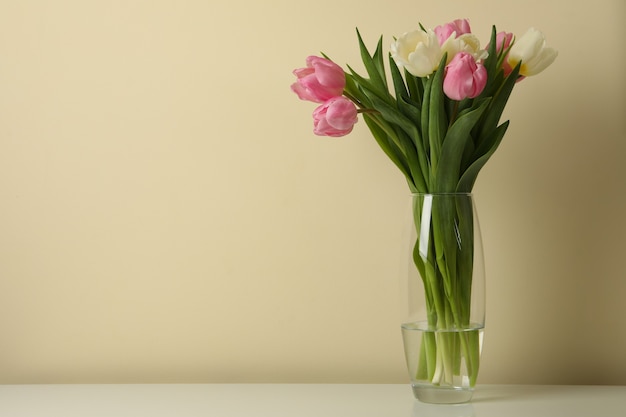 Vaas met tulpen tegen beige achtergrond, ruimte voor tekst