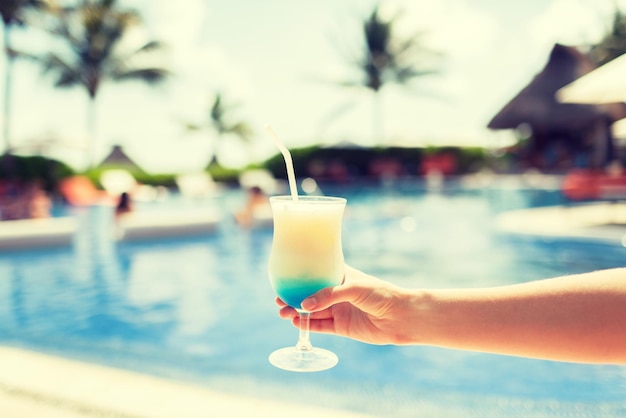 концепция отпуска, напитков и путешествий - крупный план женской руки, держащей стакан с коктейлем