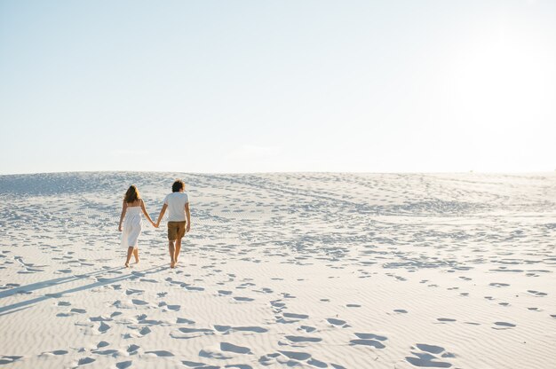 お互いに抱き合って恋をして一緒にビーチを歩いている休暇のカップル。幸せな異人種間の若いカップル。