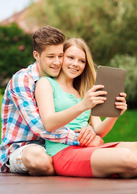 vacation, holidays, technology and friendship concept - smiling couple with tablet pc computer making selfie in park