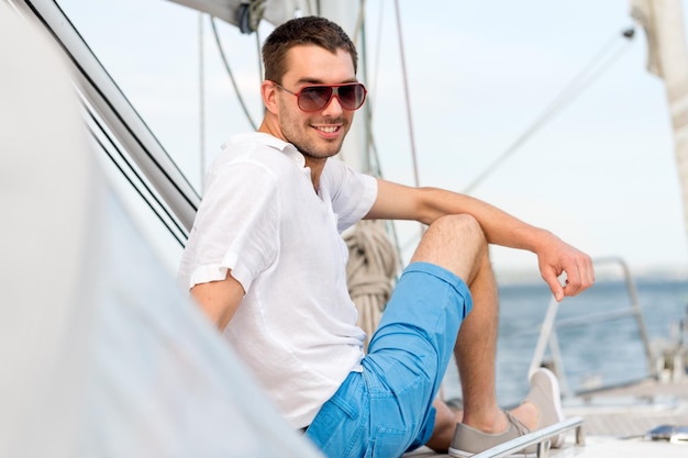 휴가, 휴일, 여행, 바다 및 사람 개념 - 요트 갑판에 앉아 선글라스를 쓴 남자