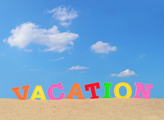 Vacation letters on a beach sand against the blue sky