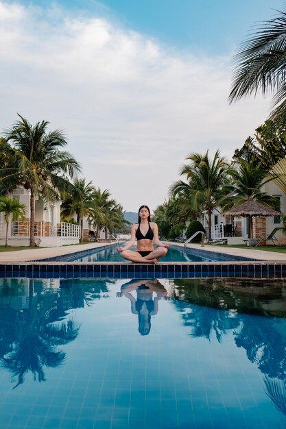 Vacation lifestyle scene of young woman sitting in swimming\
pool in morning time weekend and holiday lifestyle concept morning\
meditation by the pool