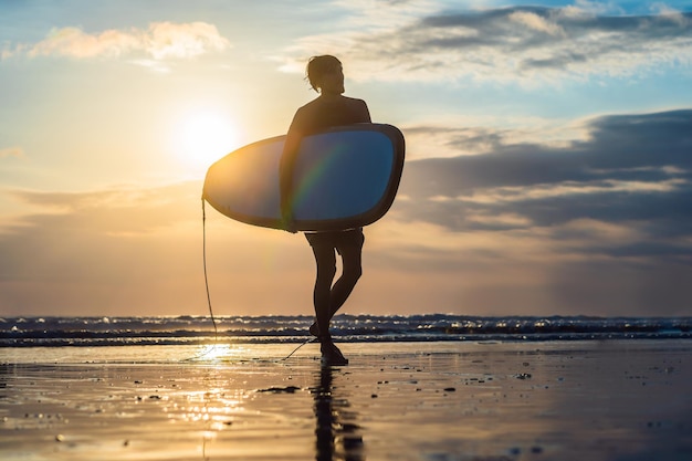 Siluetta di vacanza di un surfista che porta la sua tavola da surf a casa al tramonto con lo spazio della copia