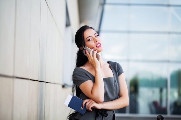 Vacanza. passeggero femminile sorridente che procede all'uscita del cancello che tira valigia attraverso il concorso dell'aeroporto