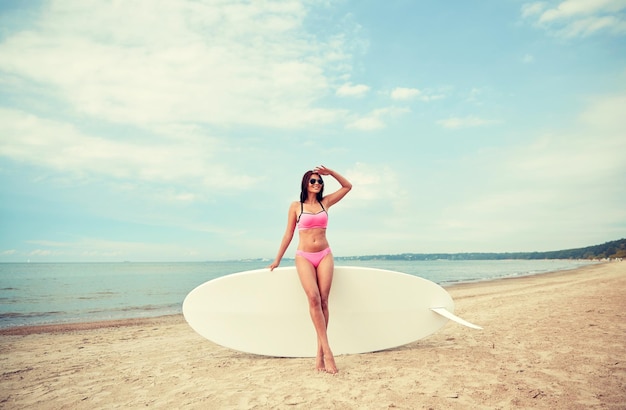 vacation, surfing, water sport and people concept - young woman in swimsuit with surfboard, windsurf or paddle board on summer beach