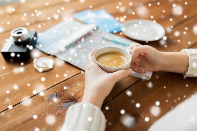 vacation, tourism, winter holidays and people concept - hands with coffee cup and travel stuff over snow