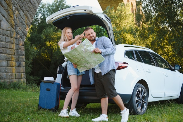 休暇、旅行-夏休みの旅行の準備ができている家族。スーツケースと車のルート。ロードトリップを計画している手に地図を持っている人。旅行のコンセプト。旅行者。