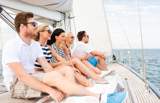 Vacation, travel, sea, friendship and people concept - smiling friends sitting on yacht deck