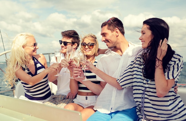 休暇、旅行、海、友情、そして人々のコンセプト-ヨットでシャンパングラスを持って友達を笑顔