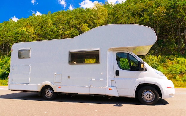 Vacation trip with Caravan Car on road. Camper and Summer drive on highway. Holiday journey in rv motorhome for recreation. Motor home minivan motion ride on nature. Scenery with mini van vehicle.
