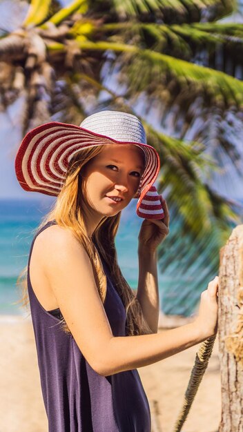 나무 다리 수직 형식에서 바다 전망을 즐기는 모자를 쓴 열대 섬 여성에서의 휴가