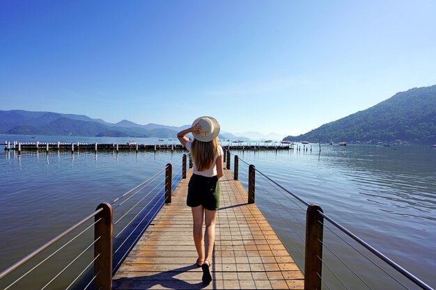 Vacation in Ubatuba Brazil Back view of young traveler woman walking on pier enjoying landscape in Ubatuba Brazil