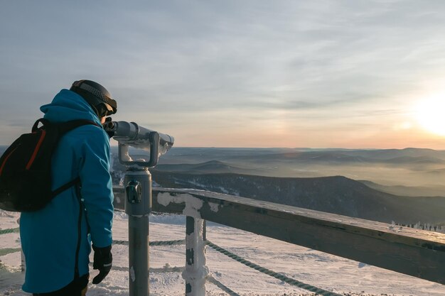 A vacationer looks through a telescope at a viewing point in a\
ski resort