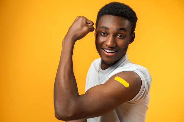 Vaccinated african american man showing his arm against yellow background