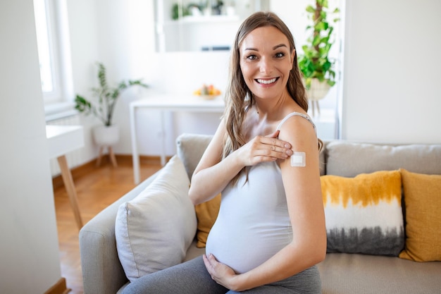Vaccinatie tegen coronavirus tijdens zwangerschap Blije zwangere dame die gevaccineerde arm toont met gipsstrip poseren na injectie van coronavirusvaccin Corona-virusimmunisatie
