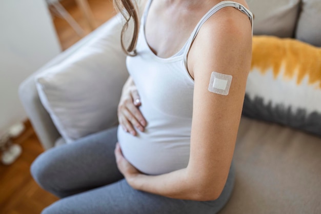 Vaccinatie tegen het coronavirus tijdens de zwangerschap. Vrolijke zwangere dame die gevaccineerde arm toont met gipsstrip poseren na injectie van coronavirusvaccin. Vaccinatie tegen corona