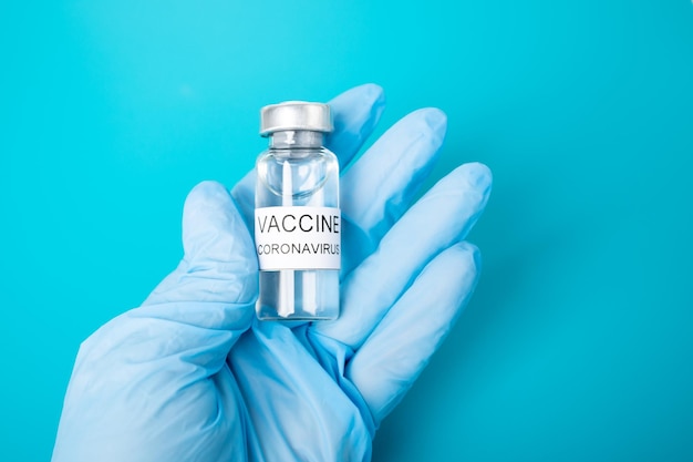 Vaccinatie van de bevolking covid19 Doctor's handen in handschoenen houden een ampul met coronavirusvaccin vast op een medische blauwe achtergrond in een kliniek