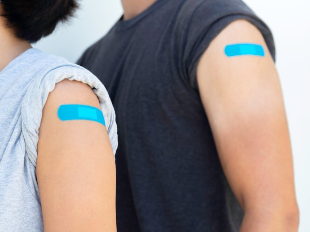Vaccinaties, verbandpleister op gevaccineerd mensenconcept. Blauwe zelfklevende verbanden op de schouder van een vrouw die een grijs shirt draagt naast een man in een donker shirt, na een vaccinatiebehandeling.