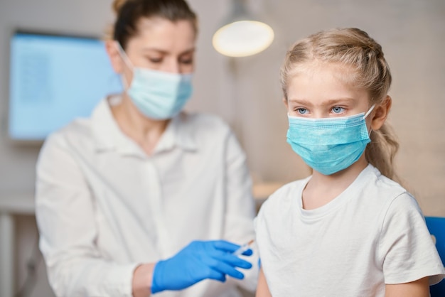 Vaccination of children A woman doctor makes injection with a syringe of a vaccine to a teenager