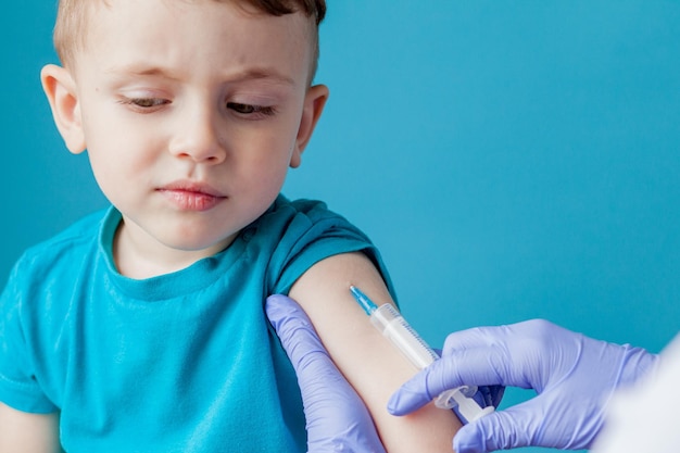 Vaccination concept Female doctor vaccinating cute little boy on blue background closeup