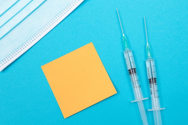 青いテーブルの上に横たわっているワクチン接種免疫学または再ワクチン接種の概念2つの医療用使い捨て注射器..。