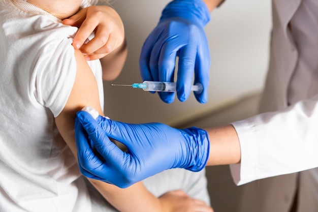 医者の予約で小さな女の子の子供たちのワクチン接種は、腕のコンスに注射します