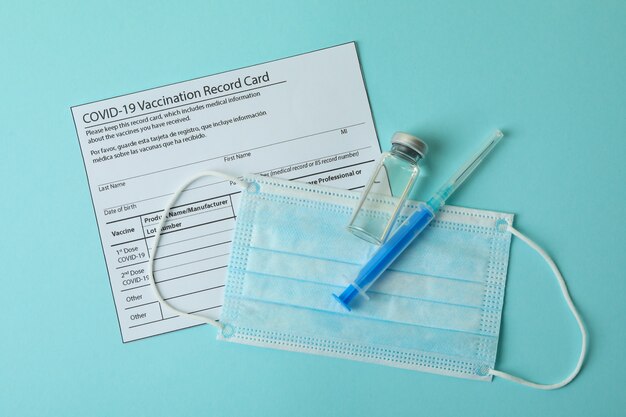 Vaccination record card, mask and syringe on blue background