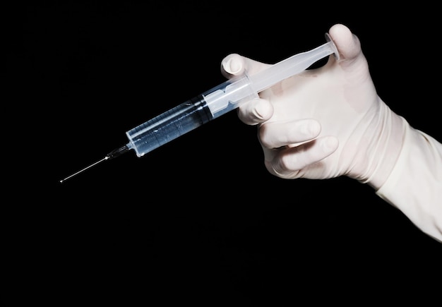 Vaccination time A hand wearing a glove holding a syringe against a black background