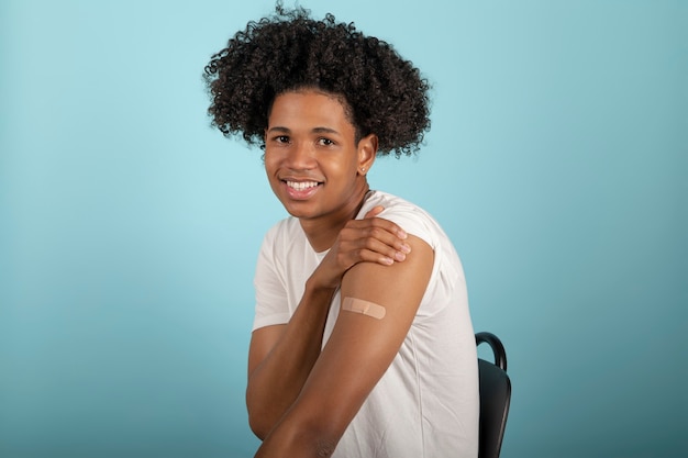 Vaccination of a young Latino man showing his arm after coronavirus vaccination on a blue background.