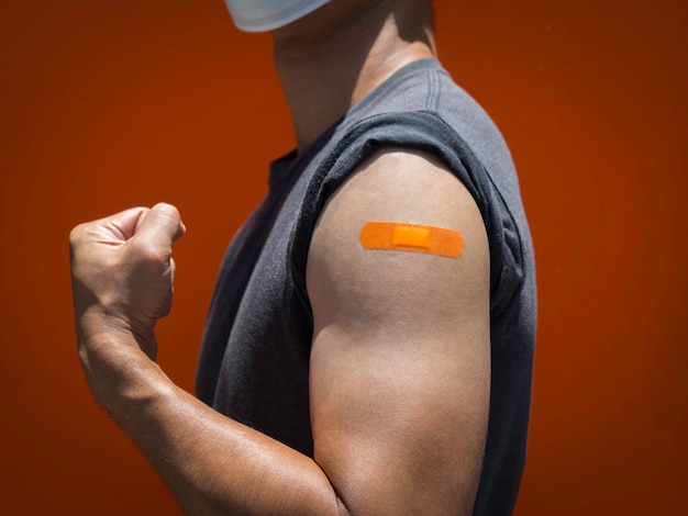 Vaccinations, bandage plaster on vaccinated people's arm concept. Orange color adhesive bandage on the strong man's arm who fist hand and showing muscle after vaccination treatment.