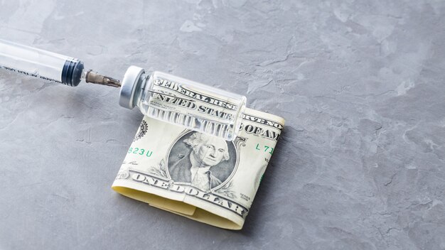 Бутылка вакцины, шприц и долларовая банкнота на сером фоне