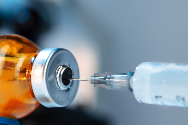 Vaccine bottle with a syringe taking the vaccine from it close up.