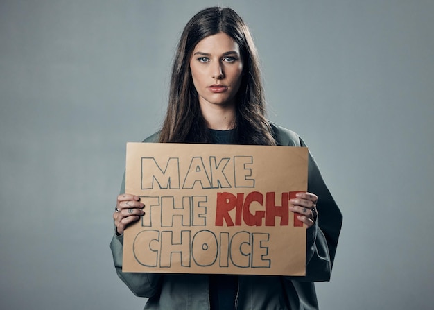 Vaccine choice and portrait of a woman with a sign isolated on a grey studio background Decision showing and girl with a poster for healthcare medical attention and safety from covid on backdrop