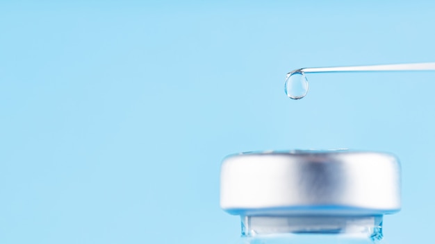 Vaccine drop on syringe needle. Needle with a drop of vaccine on a blue background