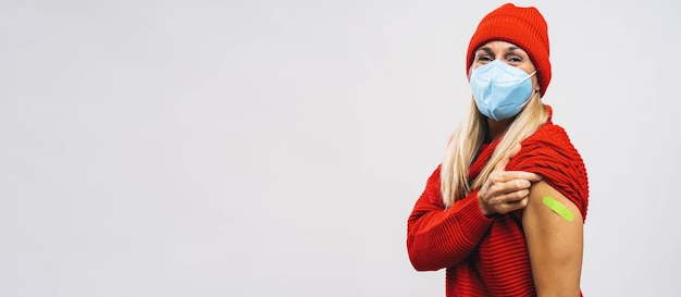 Iniezione di vaccino per il virus corona covid19 donna con maschera facciale che tiene su la manica del maglione e mostra il braccio con benda adesiva verde intonaco dopo aver ricevuto la vaccinazione banner spazio copia