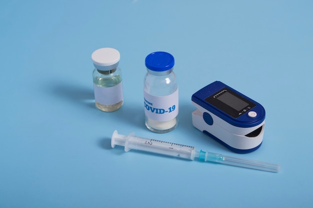 Макет вакцины или лекарства. Пульсоксиметр, вакцина против коронавируса и шприц на синем фоне. Диагностика Covid 19. Banner Pandemic 2021