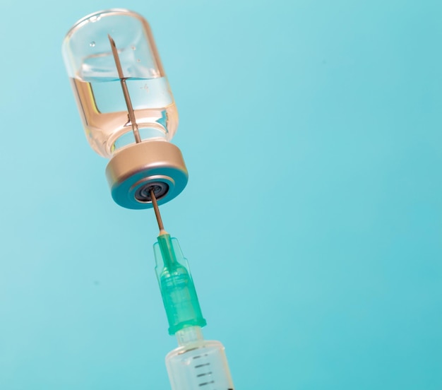 Vaccine vial dose and syringe against pale blue background