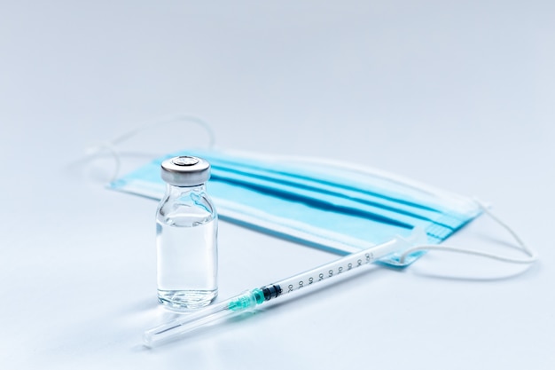 Vaccine vial, syringe and mask on white background