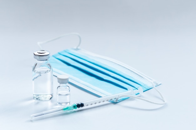 Vaccine vial, syringe and mask on white table