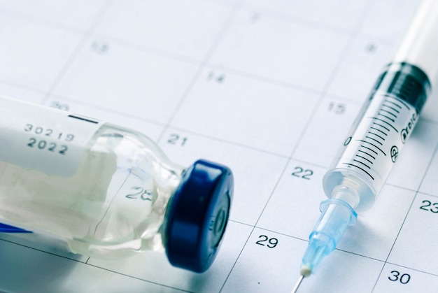 Photo vaccine vial with syringe needle on calendar