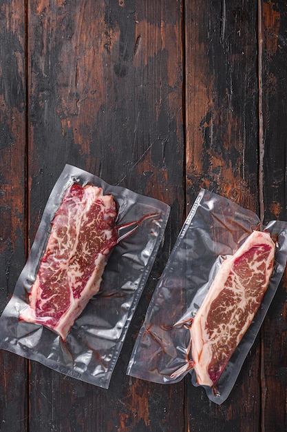 Vacuum packed meat , top blade beef steak on dark old wooden\
table, top view