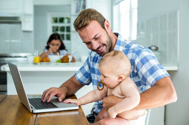 Vader die babyjongen bekijkt terwijl thuis het gebruiken van laptop